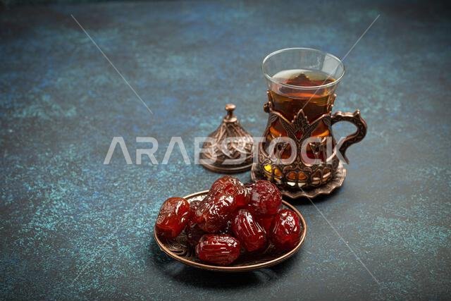 إفطار رمضاني كريم مع التمر المجفف، وجبة إفطار تتضمن التمر والشاي العربي في كوب تقليدي، منظر من زاوية مختلفة على خلفية زرقاء ريفية.