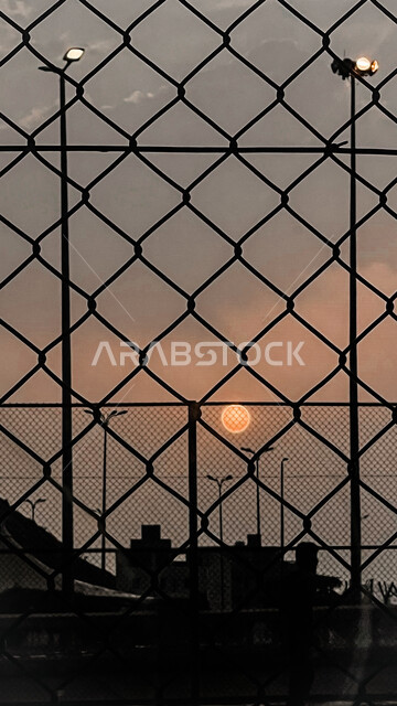 صورة مقربة لقرص الشمس بدون شعاع وقت الغروب مصور من سياج حديدي 