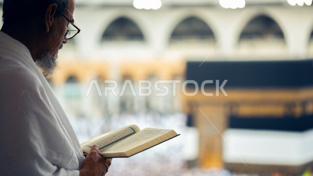 A picture from the back of a man in the Great Mosque of Mecca wearing Ihram clothes and reading the Qur’an, praying and supplicating in the Grand Mosque, worshiping and getting closer to God, reading and reciting the Qur’an, worshiping in the homes of God