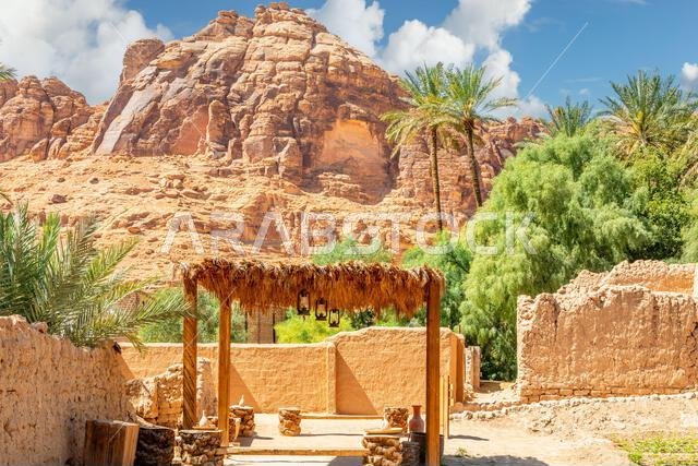 Al Ula ruined old town streets with straw sunshade tent and palms with mountains in the background, Saudi Arabia