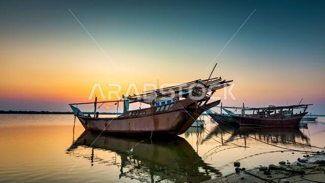 تضفي الألوان الذهبية رونقاً على شاطئ الدمام الهادئ بينما تستريح القوارب في ضوء الصباح، في مشهد يجسد جمال الطبيعة في المملكة العربية السعودية.
