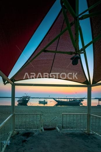 Golden hues paint the tranquil Dammam seaside as boats rest against the morning glow, a serene embrace of nature's beauty in Saudi Arabia.