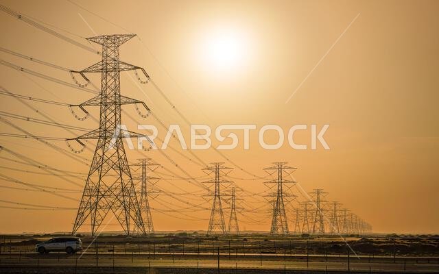 Large tall steel power pylons in rather flat landscape of Saudi Arabia, only black silhouettes visible against bright afternoon sun