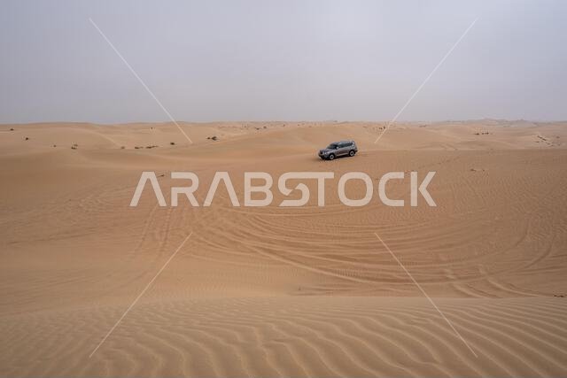 SUV four wheel drive vehicle car Al Qudra empty quarter seamless desert sahara in Dubai UAE middle east with wind paths and sand hills gray cloudy sky