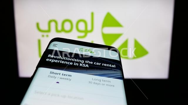 هاتف محمول يعرض موقع شركة لومي السعودية لتأجير السيارات على الشاشة أمام شعار الشركة. التركيز على الزاوية العلوية اليسرى من شاشة الهاتف. هاتف محمول يعرض موقع شركة لومي السعودية لتأجير السيارات على الشاشة أمام شعار الشركة. التركيز على الزاوية العلوية اليسرى من شاشة الهاتف.