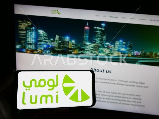 Person holding smartphone with logo of Saudi Arabian car rental company Lumi on screen in front of website. Focus on phone display.