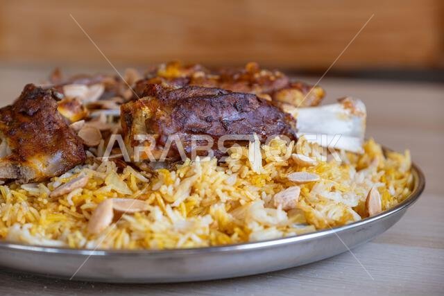 Plate of meat and rice topped with almonds on wooden table with top view