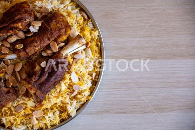 Plate of meat and rice topped with almonds on wooden table with top view