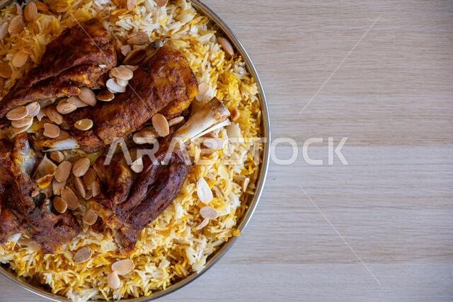 Plate of meat and rice topped with almonds on wooden table with top view