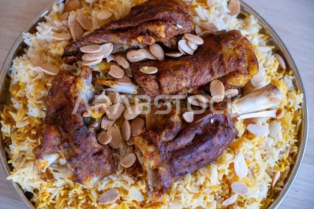 Plate of meat and rice topped with almonds on wooden table with top view