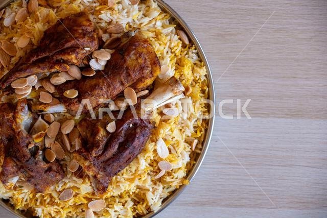 Plate of meat and rice topped with almonds on wooden table with top view