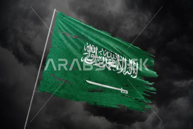 علم المملكة العربية السعودية ممزق على خلفية سماء داكنة.