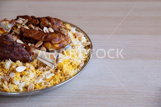 Plate of meat and rice topped with almonds on wooden table with top view