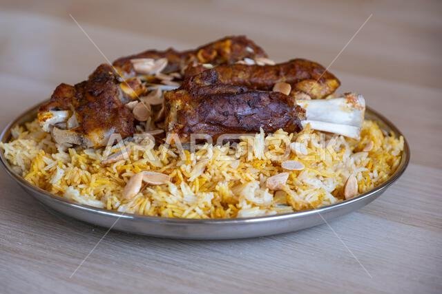 Plate of meat and rice topped with almonds on wooden table with top view