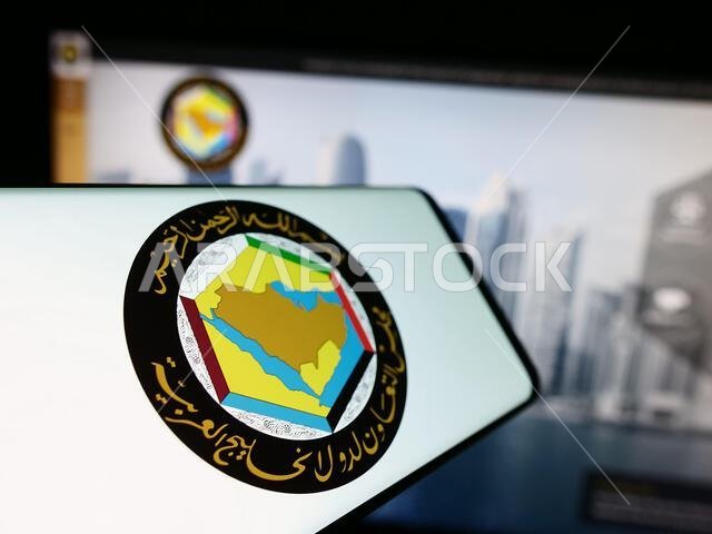 هاتف ذكي يحمل شعار الاتحاد العربي ومجلس التعاون الخليجي أمام موقع إلكتروني. التركيز على منتصف يسار شاشة الهاتف.