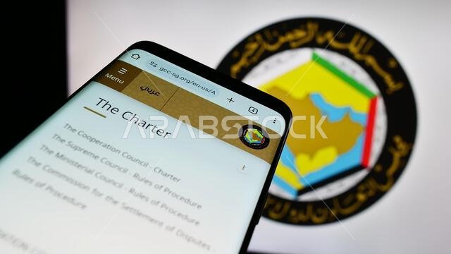 هاتف محمول يعرض موقع مجلس التعاون الخليجي أمام شعاره. ركّز على الزاوية العلوية اليسرى من شاشة الهاتف.