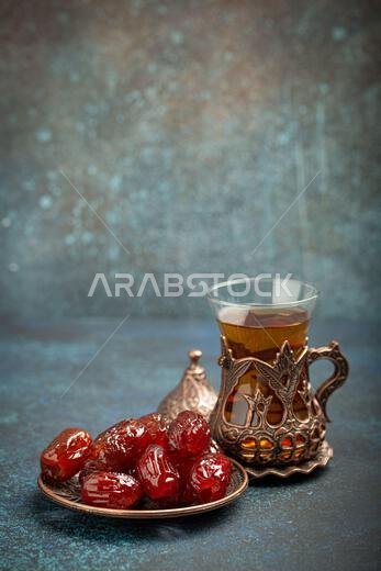Breaking fasting with dried dates during Ramadan Kareem, Iftar meal with dates and Arab tea in traditional glass, angle view on rustic blue background