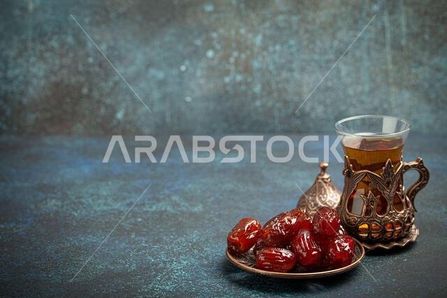 إفطار رمضاني كريم مع التمر المجفف، وجبة إفطار تتضمن التمر والشاي العربي في كوب تقليدي، منظر من زاوية مختلفة على خلفية زرقاء ريفية.