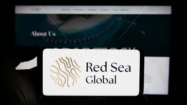 Person holding smartphone with logo of Saudi Arabian development company Red Sea Global in front of website. Focus on phone display. Person holding smartphone with logo of Saudi Arabian development company Red Sea Global in front of website. Focus on phone display.