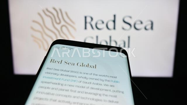 هاتف ذكي يعرض موقع شركة التطوير العقاري السعودية "البحر الأحمر العالمي" أمام شعار الشركة. التركيز على أعلى يسار شاشة الهاتف. هاتف ذكي يعرض موقع شركة التطوير العقاري السعودية "البحر الأحمر العالمي" أمام شعار الشركة. التركيز على أعلى يسار شاشة الهاتف.
