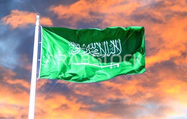 Flag of Saudi Arabia waving in the wind against the red sunset sky