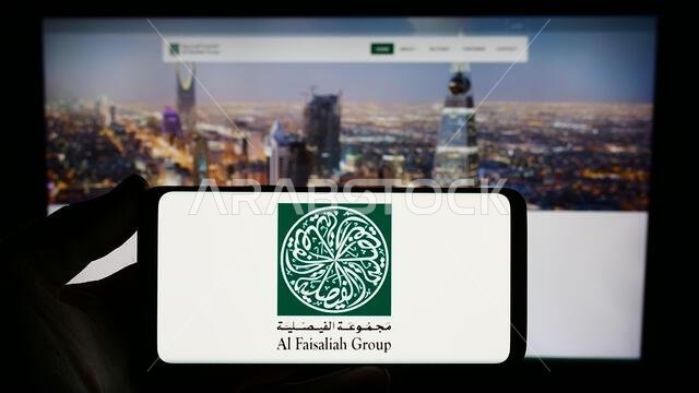 Person holding smartphone with logo of Saudi Arabian company Al Faisaliah Group in front of website. Focus on phone display.