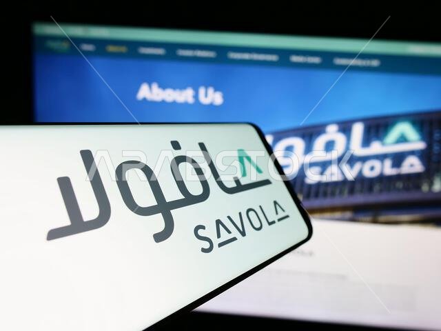هاتف ذكي يحمل شعار شركة سافولا جروب الصناعية السعودية أمام موقعها الإلكتروني. التركيز على منتصف شاشة الهاتف.
