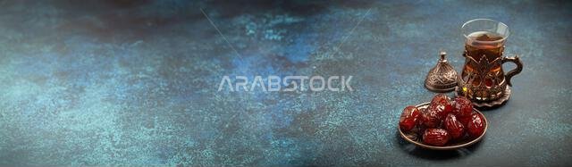 Breaking fasting with dried dates during Ramadan Kareem, Iftar meal with dates and Arab tea in traditional glass, angle view on rustic blue background