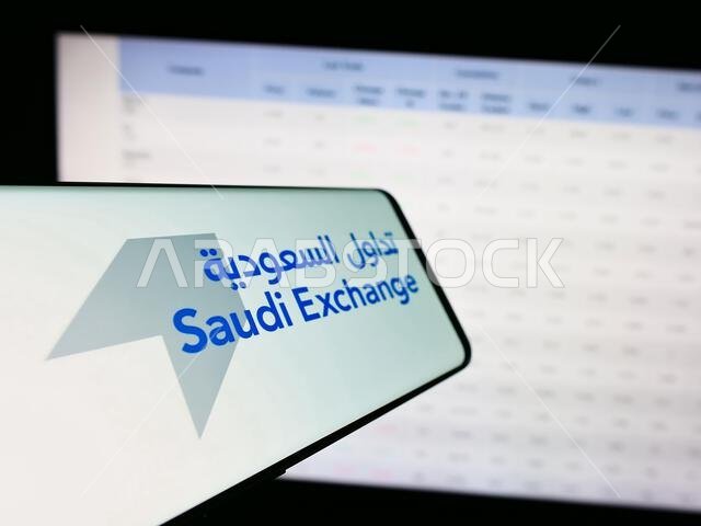 Smartphone with logo of Arabian stock exchange Saudi Exchange (Tadawul) in front of company website. Focus on center-left of phone display.