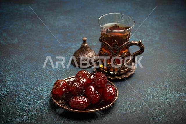 إفطار رمضاني كريم مع التمر المجفف، وجبة إفطار تتضمن التمر والشاي العربي في كوب تقليدي، منظر من زاوية مختلفة على خلفية زرقاء ريفية.