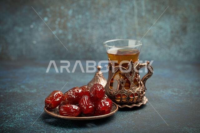 إفطار رمضاني كريم مع التمر المجفف، وجبة إفطار تتضمن التمر والشاي العربي في كوب تقليدي، منظر من زاوية مختلفة على خلفية زرقاء ريفية.