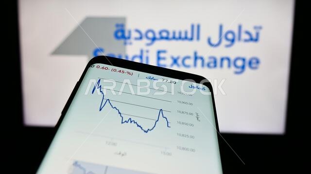 هاتف محمول يعرض موقع بورصة السعودية (تداول) أمام شعار الشركة. ركّز على الزاوية العلوية اليسرى من شاشة الهاتف. هاتف محمول يعرض موقع بورصة السعودية (تداول) أمام شعار الشركة. ركّز على الزاوية العلوية اليسرى من شاشة الهاتف.