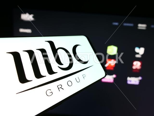 Smartphone with logo of Saudi Arabian media company MBC Group in front of website. Focus on center-left of phone display. Smartphone with logo of Saudi Arabian media company MBC Group in front of website. Focus on center-left of phone display.