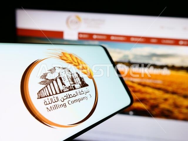 هاتف محمول يحمل شعار شركة الطحن السعودية رقم 3 (MC3) على الشاشة أمام موقع إلكتروني. التركيز على منتصف يمين شاشة الهاتف.