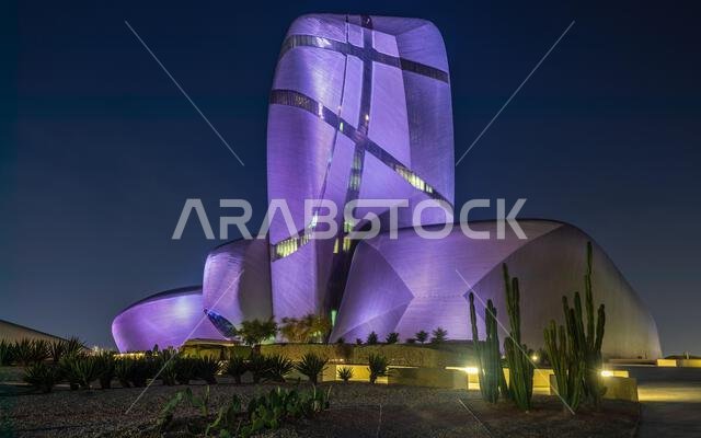 Illuminated during the night modern building in the center of Al Khobar with green cactuses in the foreground, Saudi Arabia