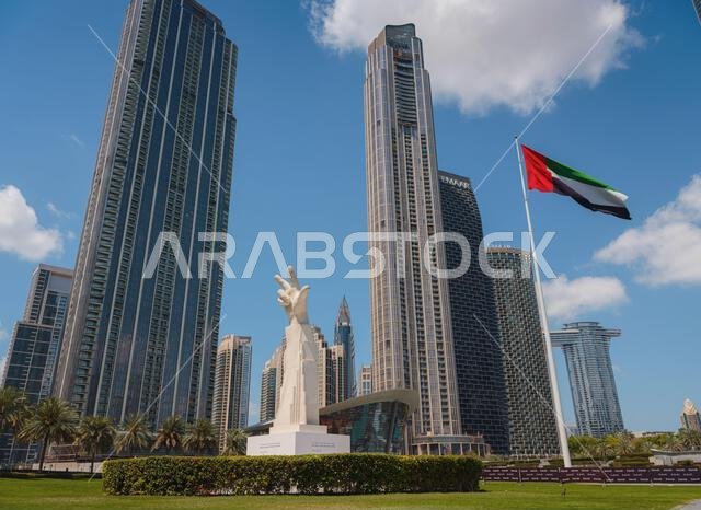 20 مارس 2023، دبي، الإمارات العربية المتحدة: تمثال الأصابع الثلاثة بالقرب من علم الإمارات في يوم مشمس، وبرج خليفة، أطول ناطحة سحاب في العالم، في دولة الإمارات العربية المتحدة.
