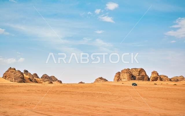 Typical desert landscape in Alula, Saudi Arabia, sand with some mountains, small offroad vehicle, local man and camels at distance