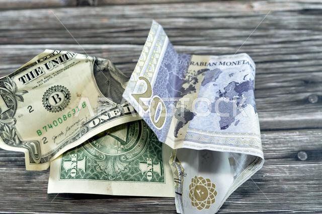عملة سعودية مجعدة ومتكسرة من فئة 20 ريالاً سعودياً ودولار أمريكي واحد، تضخم العملة وفقدان قيمتها، مفهوم الانخفاض.