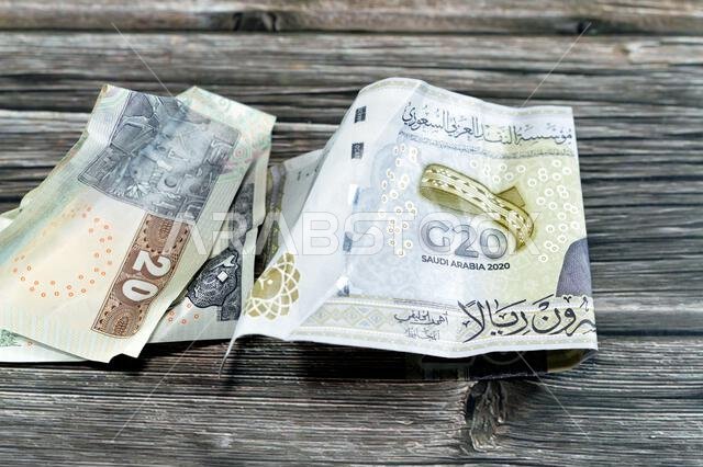 ورقة نقدية مصرية مجعدة من فئة 20 جنيهاً مصرياً، وورقة نقدية سعودية من فئة 20 ريالاً سعودياً عليها شعار قمة مجموعة العشرين، وأوراق نقدية مجعدة، وأوراق نقدية سعودية ومصرية