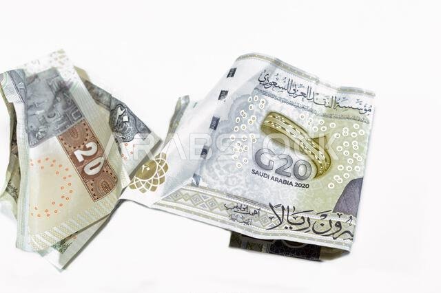 ورقة نقدية مصرية مجعدة من فئة 20 جنيهاً مصرياً، وورقة نقدية سعودية من فئة 20 ريالاً سعودياً عليها شعار قمة مجموعة العشرين، وأوراق نقدية مجعدة، وأوراق نقدية سعودية ومصرية