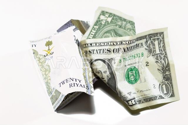 عملة سعودية مجعدة ومتكسرة من فئة 20 ريالاً سعودياً ودولار أمريكي واحد، تضخم العملة وفقدان قيمتها، مفهوم الانخفاض.