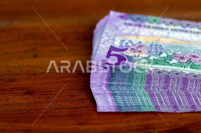 A pile of Saudi Arabia five riyals banknotes money on wooden table, selected focus