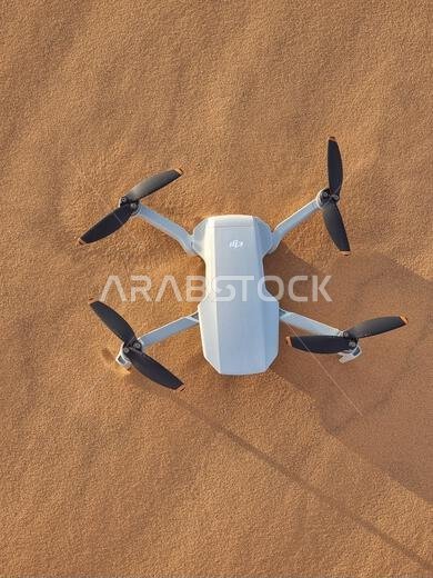 A vertical shot of a  white drone on the  sand on a sunny day in Saudi Arabia