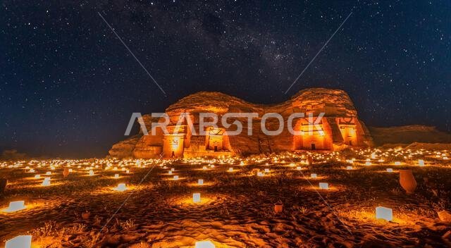 Starlight sky over the ancient nabataean tombs of Hegra city illuminated, night panorama, Al Ula, Saudi Arabia