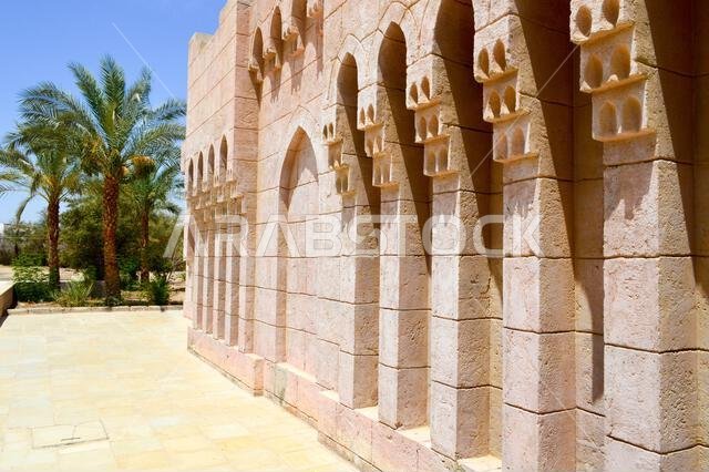 Brick old ancient carved Arab Islamic Islamic wall with ornaments and patterns against the background of green tropical palm trees.
