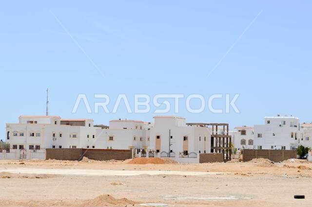 بيوت عربية بيضاء مستطيلة الشكل في الصحراء بنوافذ تتناقض مع خلفية الرمال الصفراء والسماء الزرقاء.