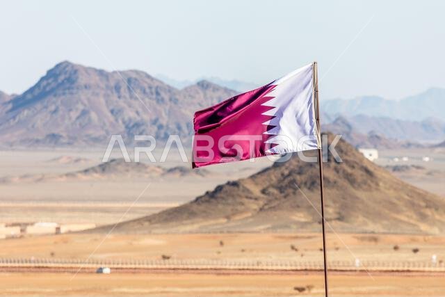 Qatar flag waving on the wind in Saudi Arabian desertwith mountains in background, Al Ula, Saudi Arabia Qatar flag waving on the wind in Saudi Arabian desertwith mountains in background, Al Ula, Saudi Arabia