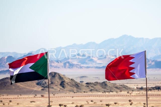 Sudanese and Bahrain flags waving togetner on the wind in Saudi Arabian desertwith mountains in background, Al Ula, Saudi Arabia
