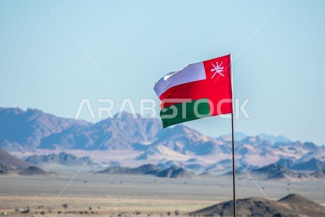Omani flag waving on the wind in Saudi Arabian desertwith mountains in background, Al Ula, Saudi Arabia Omani flag waving on the wind in Saudi Arabian desertwith mountains in background, Al Ula, Saudi Arabia