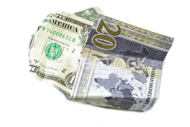 عملة سعودية مجعدة ومتكسرة من فئة 20 ريالاً سعودياً ودولار أمريكي واحد، تضخم العملة وفقدان قيمتها، مفهوم الانخفاض.